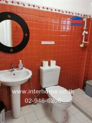 Bathroom with red tiled wall, round mirror, sink, and toilet