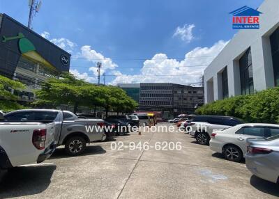 Parking area of a commercial building with multiple cars parked and surrounding buildings under clear sky