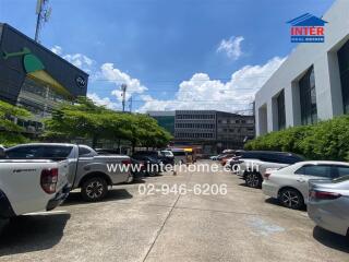 Parking area of a commercial building with multiple cars parked and surrounding buildings under clear sky