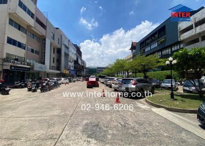 Parking area in front of various buildings with cars and motorcycles parked