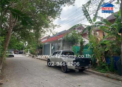 Street view of a residential building with trees and a parked truck.