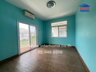 Vacant bedroom with wooden floor, blue walls, large windows, and balcony access