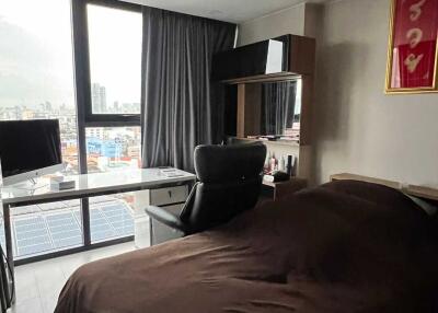 A bedroom with a bed, desk, chair, and large window with a city view