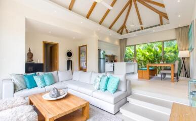 Spacious living room with modern decor, wooden beams on ceiling, open plan kitchen, and dining area with a view of greenery