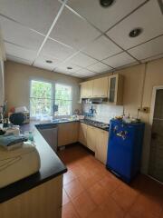 A functional kitchen with wooden cabinets, stove, and refrigerator, well-lit by a large window