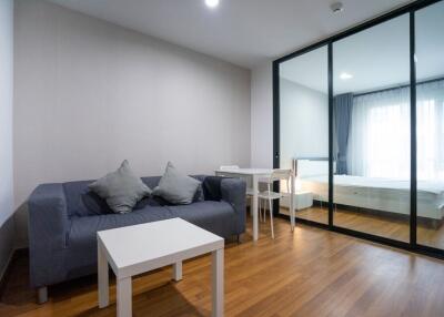 Modern living room with a sofa and coffee table adjacent to a bedroom separated by glass sliding doors