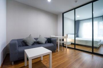 Modern living room with a sofa and coffee table adjacent to a bedroom separated by glass sliding doors