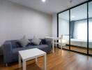 Modern living room with a sofa and coffee table adjacent to a bedroom separated by glass sliding doors