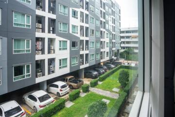 View of the apartment building from a window showing cars parked and greenery