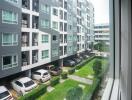 View of the apartment building from a window showing cars parked and greenery