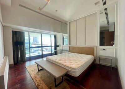 Spacious bedroom with a large bed, wooden flooring, and a large window with city view