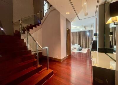 Elegant hallway and staircase with hardwood flooring leading to a bright living area