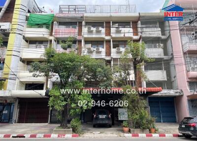 Exterior view of a multi-story residential building with parked cars and trees.