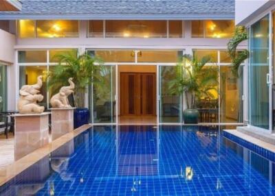 View of a luxurious house with a blue-tiled swimming pool surrounded by greenery and sculptures