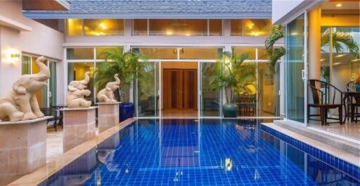 View of a luxurious house with a blue-tiled swimming pool surrounded by greenery and sculptures