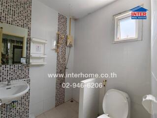 Small white-tiled bathroom with a shower, sink, and toilet