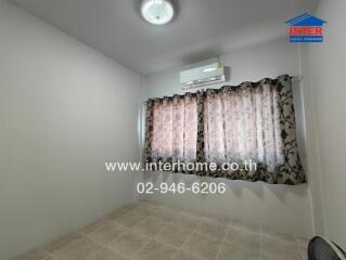 A small bedroom with tiled floor, window with patterned curtains, air conditioner, and ceiling light.