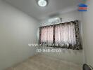 A small bedroom with tiled floor, window with patterned curtains, air conditioner, and ceiling light.