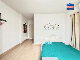 Bedroom with cartoon wall art, teal bedspread, wooden floor, and white walls