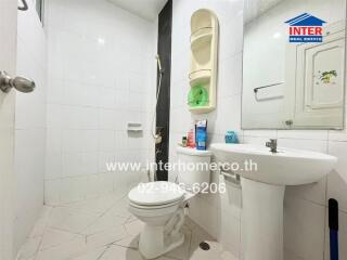 Bathroom with white tiles and fixtures, including a sink, toilet, and shower