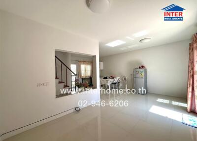 Spacious living area with ample natural light featuring a staircase, dining table, and refrigerator.