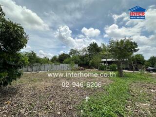 Vacant lot with surrounding greenery and a distant building