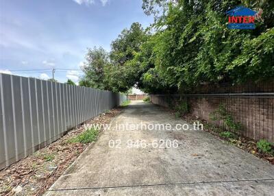 Long concrete driveway with greenery and fence on both sides