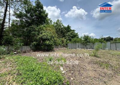 Vacant land plot surrounded by trees with clear skies, enclosed by a fence