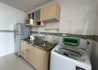 Modern kitchen with washing machine, fridge, microwave, and wooden cabinets