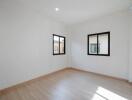 Empty bedroom with wooden floor and two windows