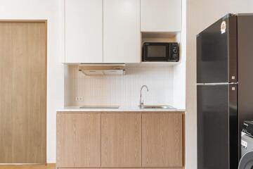 Modern kitchen with wooden cabinets, black refrigerator, and microwave.