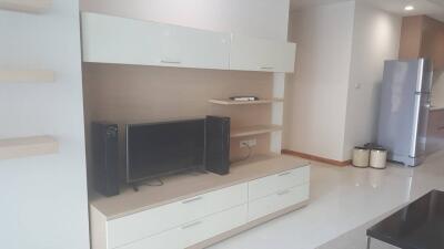 Modern living room with built-in storage, TV, and kitchen in the background