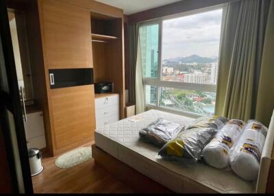Small furnished bedroom with large window and wooden storage unit