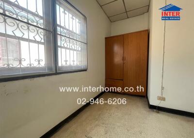 Small bedroom with a wooden wardrobe, tiled floor, and two barred windows.