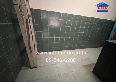 Utility area in a property with tiled walls and floor, ladder, and black cabinet