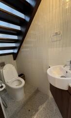 Compact bathroom with white tiles, toilet, and sink under a staircase