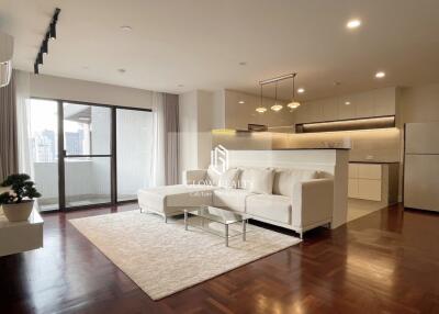 Spacious living room with a white sofa, glass coffee table, and open kitchen in the background