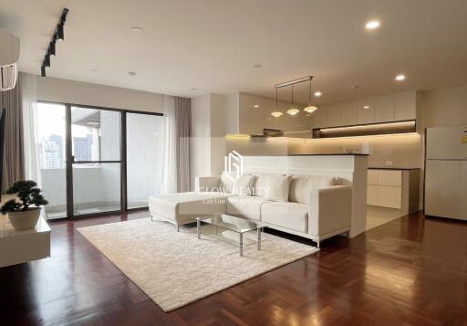 Spacious living room with a white sofa, glass coffee table, and open kitchen in the background