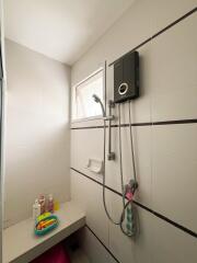 Bathroom shower area with electric water heater and toiletry shelf