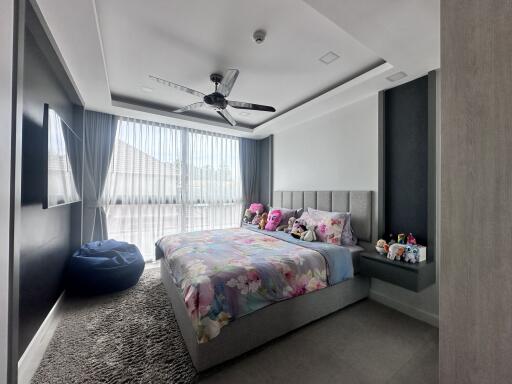 Modern bedroom with a large window, ceiling fan, and plush decorations
