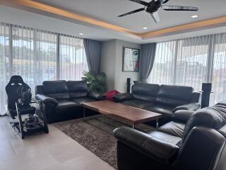 Modern living room with black leather sofas, a coffee table, large windows, and a racing simulator setup