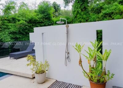 Outdoor shower next to a pool surrounded by lush greenery