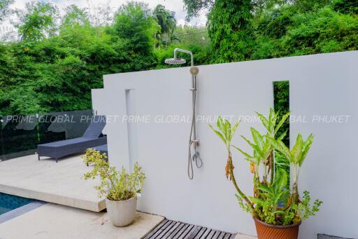 Outdoor shower next to a pool surrounded by lush greenery