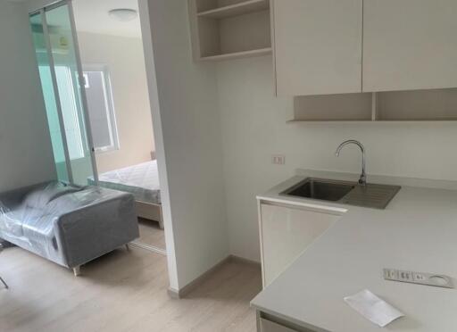 Modern kitchen and living area with bed, covered sofa, and sink.