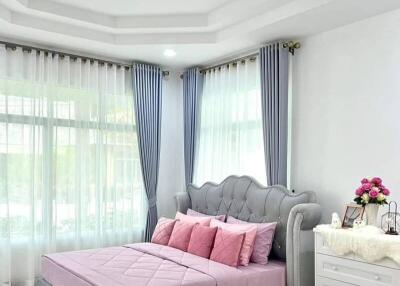 Spacious bedroom with a modern design, featuring large windows, a comfortable bed with pink bedding, and elegant curtains