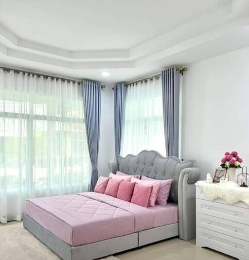 Spacious bedroom with a modern design, featuring large windows, a comfortable bed with pink bedding, and elegant curtains