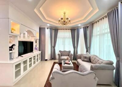 Elegant living room with chandelier, plush sofas, entertainment center, and large windows