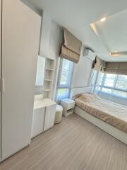 A cozy and bright modern bedroom with a large window, a bed, wardrobe, and a small vanity area