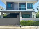 Modern two-story house with a balcony, large windows, and gated driveway