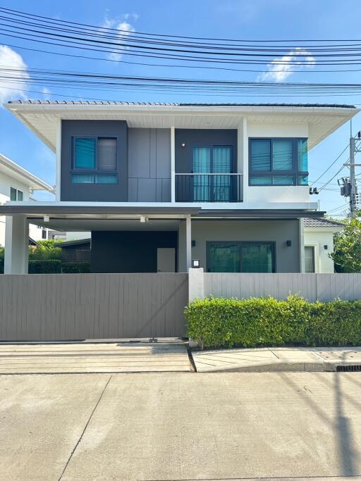 Modern two-story house with a balcony, large windows, and gated driveway